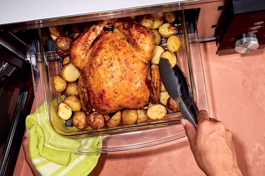 A chicken and potatoes cooked in the glass air fryer of the Ninja Crispi microwave.